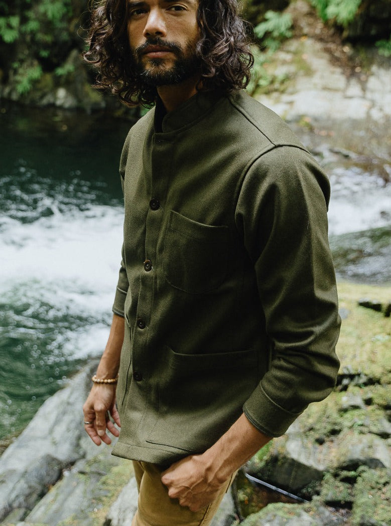 Tambo Wool Jacket in Olive Green buttoned to the band collar, worn by a river