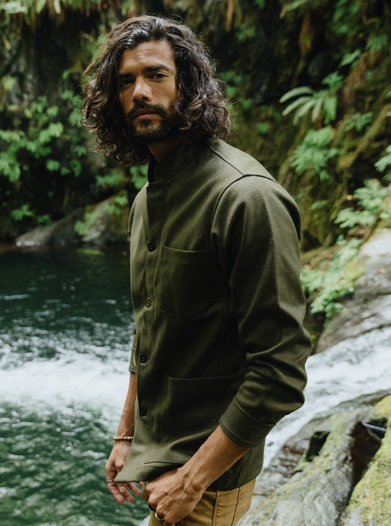 Tambo Wool Jacket in Olive Green worn beside a river in a green forest