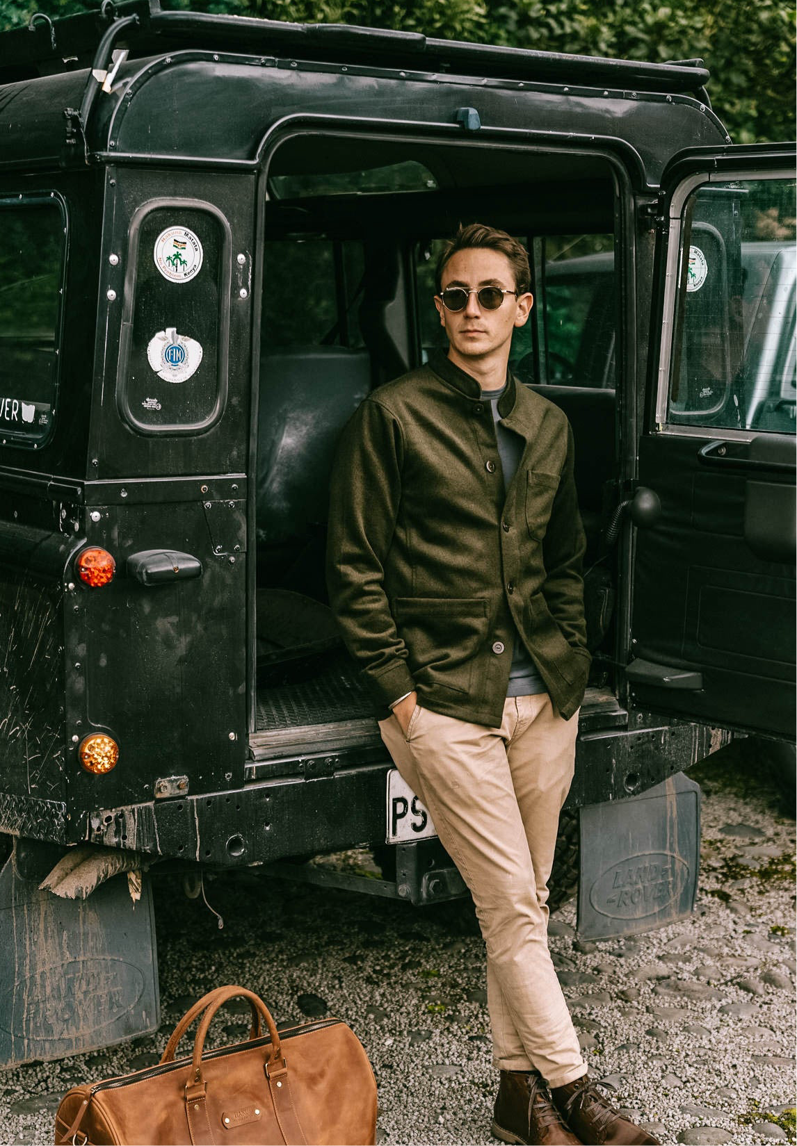 Man in sunglasses wearing the Tambo Wool Jacket in Olive Green, leaning on an open 4x4 with a leather bag